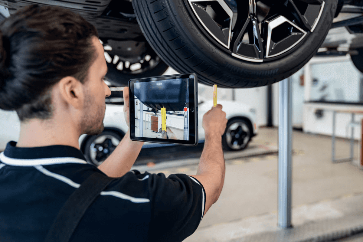 Technician measuring tire tread depth while recording the inspection on a tablet
