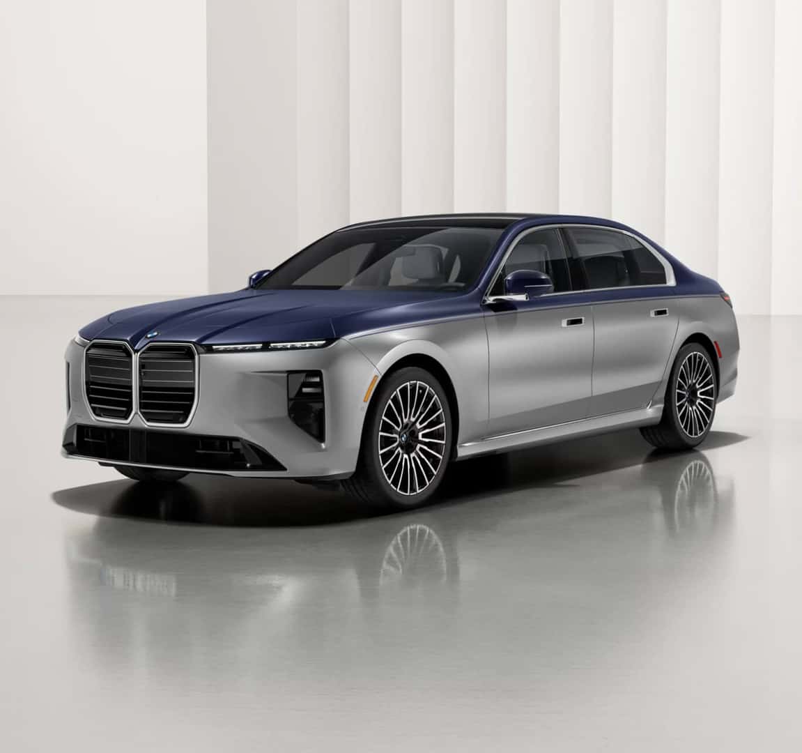 Exterior three-quarter view of a silver and blue BMW 7 Series Sedan parked in a bright minimal showroom.