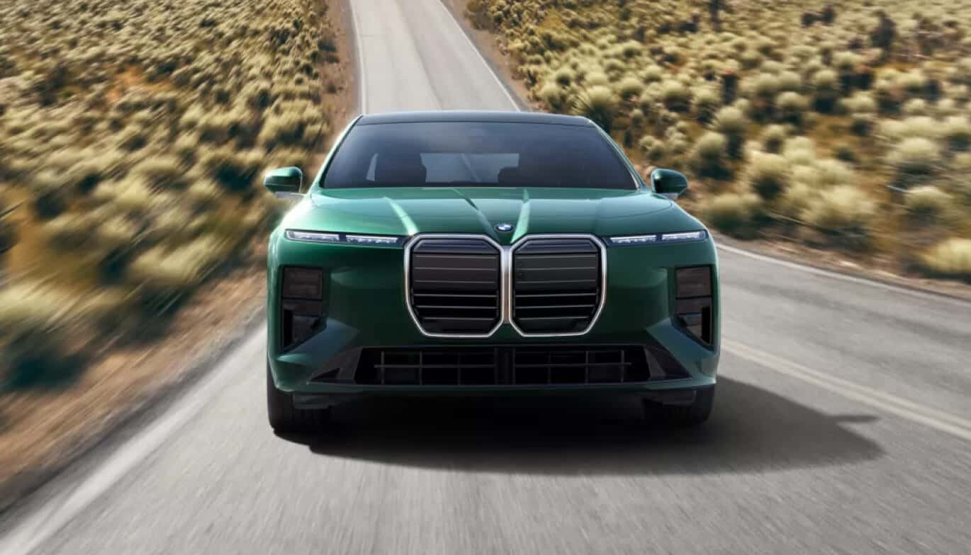 Exterior front action shot of a green BMW 7 Series driving down a two-lane desert highway.