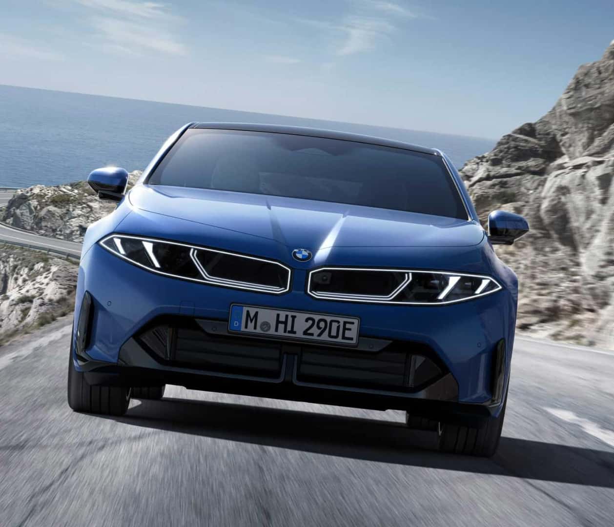 A front view action shot of a blue BMW i3 driving down an oceanside highway.