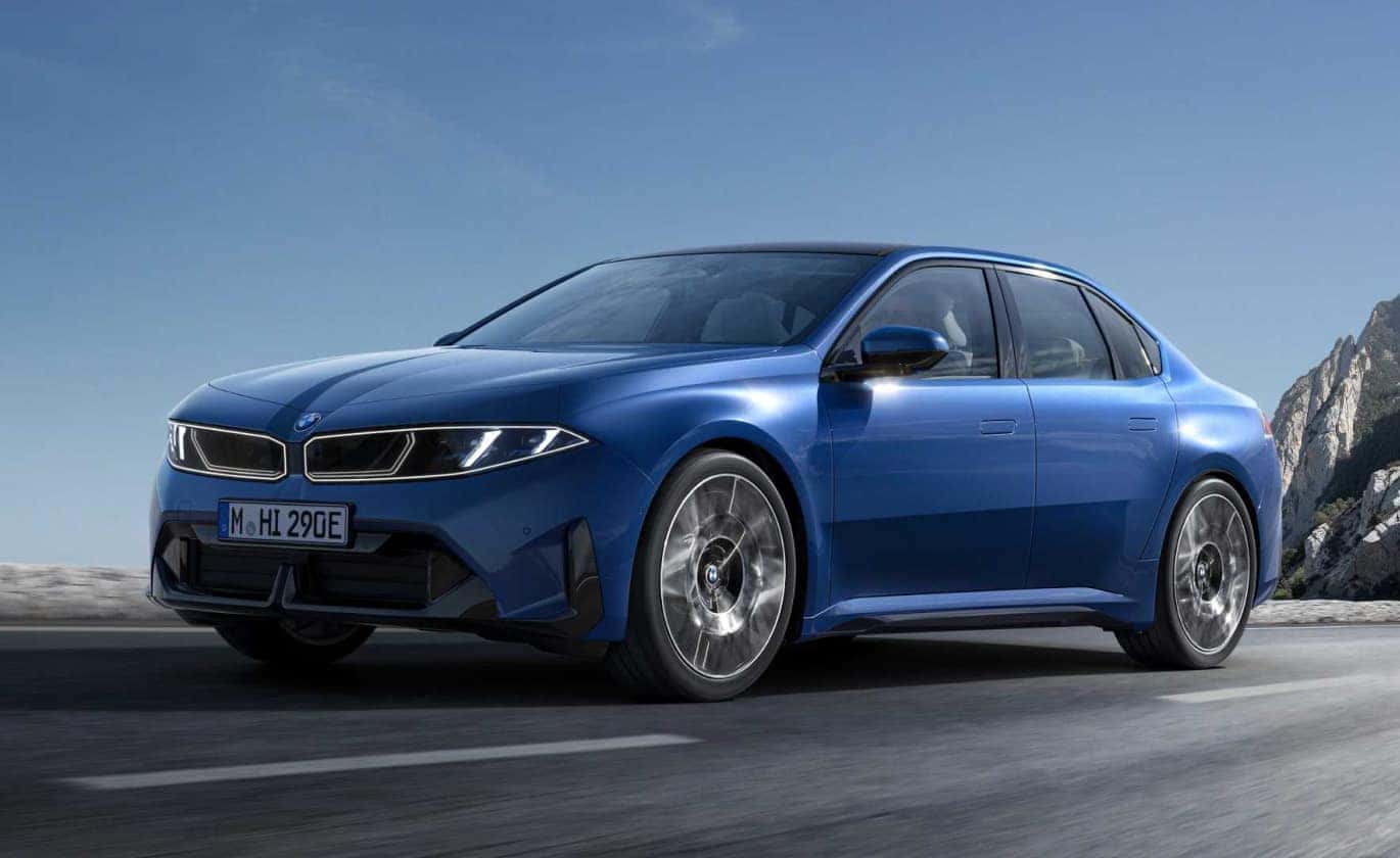 A low angle front three-quarter view action shot of a blue BMW i3 driving down a sunny highway.