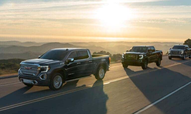 Line of GMC Sierra 1500 trucks on highway by sunrise
