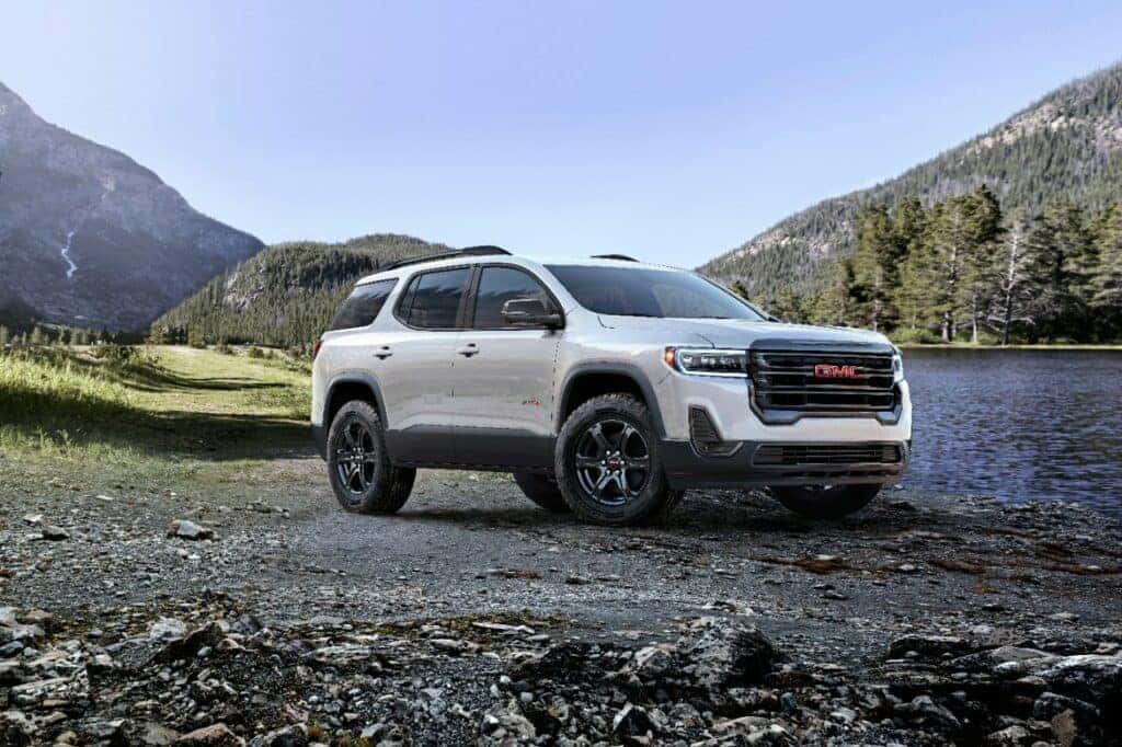 Front driver 3/4 view of 2023 GMC Acadia AT4 in Summit White with mountains and lake in background.