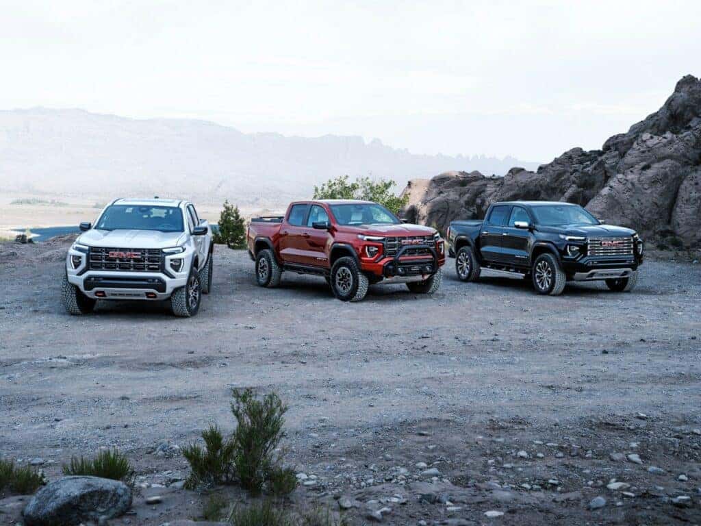 Group shot of GMC AT4, AT4X Edition 1 and Denali (L-R) all shown from front 3/4 view in desert and mountain scene.