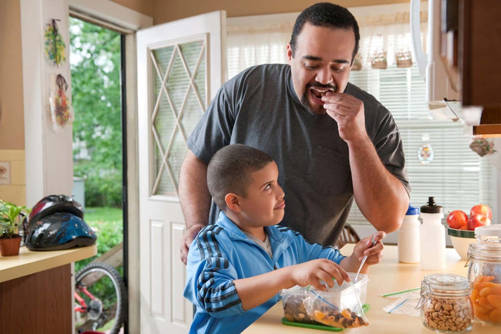 A Father Playfully Taking A Bite Of His Son's Trail Mix, A Healthy Snack