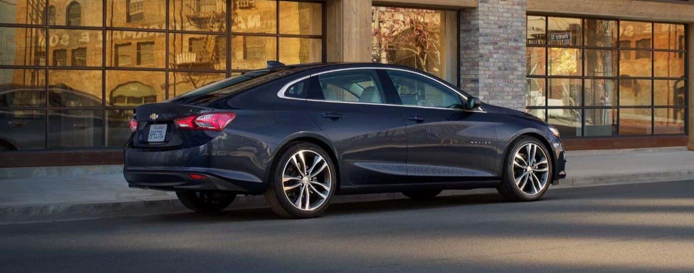 Black 2023 Chevy Malibu parked in front of a glass building.
