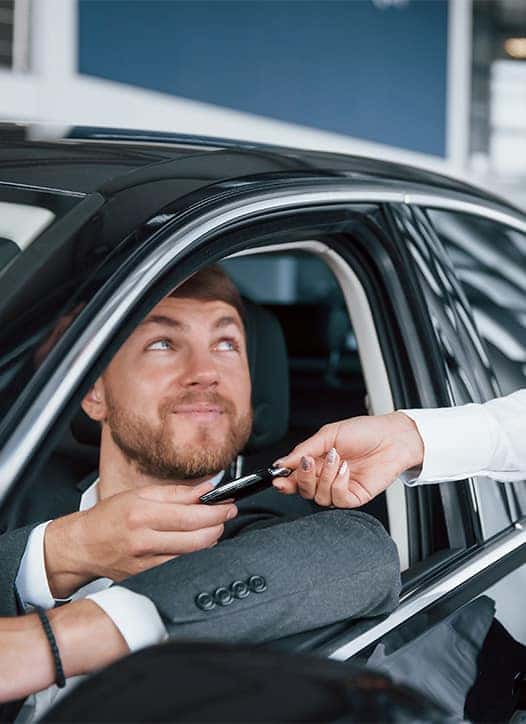 Leasing versus Buying a Chevrolet at Delaney Chevrolet of Greensburg in Greensburg, PA | Sales person handing over new car keys to customer sitting in the drivers seat of car