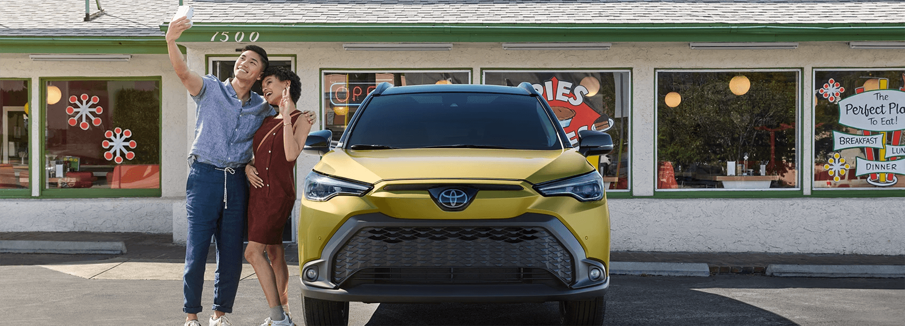 Two people taking a picture next to a 2023 Corolla Cross Hybrid