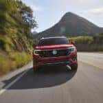 Red 2025 Volkswagen Atlas R-Line driving on a tree-lined road.