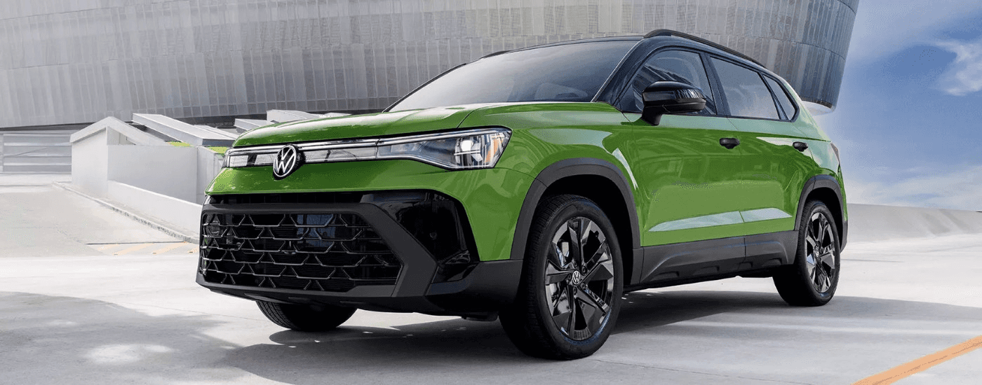 A green 2025 Volkswagen Taos parked in front of a modern building.