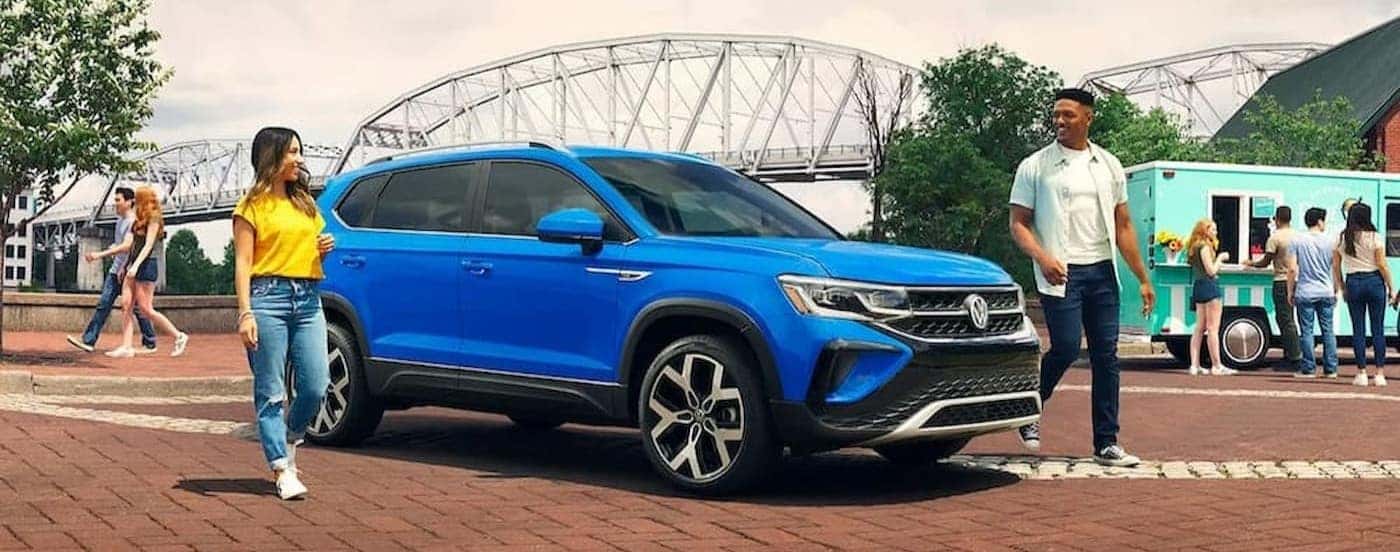 Two people walking near a blue 2023 Volkswagen Taos.
