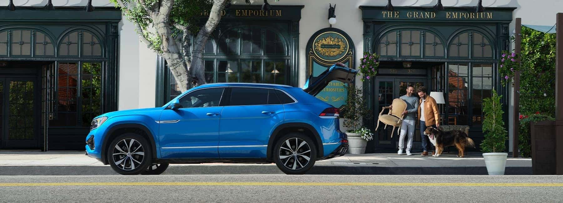 Two people and their dog loading the trunk of a blue 2024 Volkswagen Atlas Cross Sport