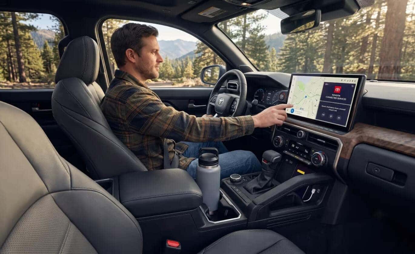 Interior image of a driver in a 2026 Tacoma touching the infotainment system.