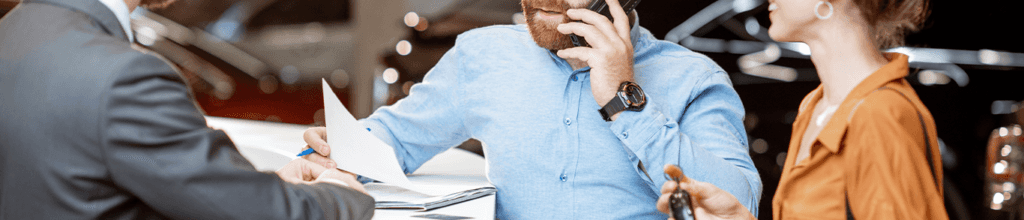 Vehicle Registration Taxes and Fees at Jack Giambalvo Buick GMC in York, PA | Couple together at dealership looking at paper work while the man in blue shirt is making a phone call