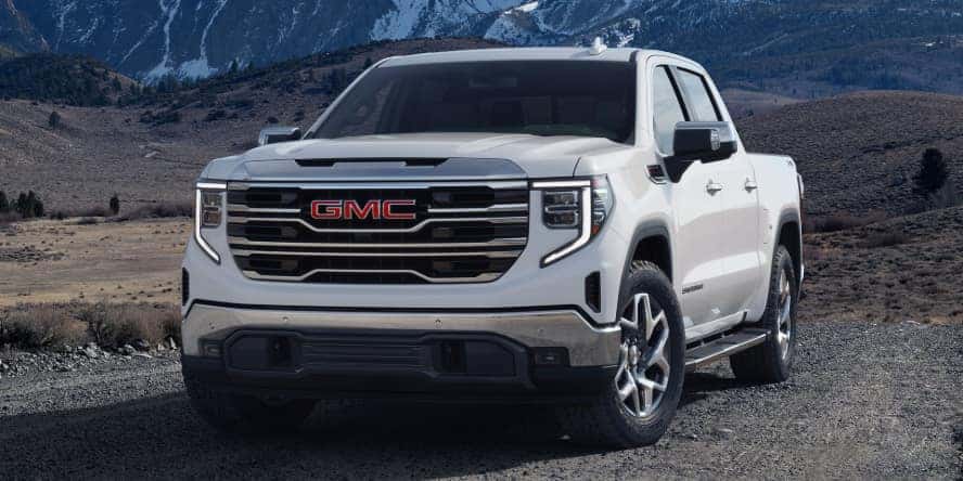 A white GMC Sierra 1500 driving on a dirt road.