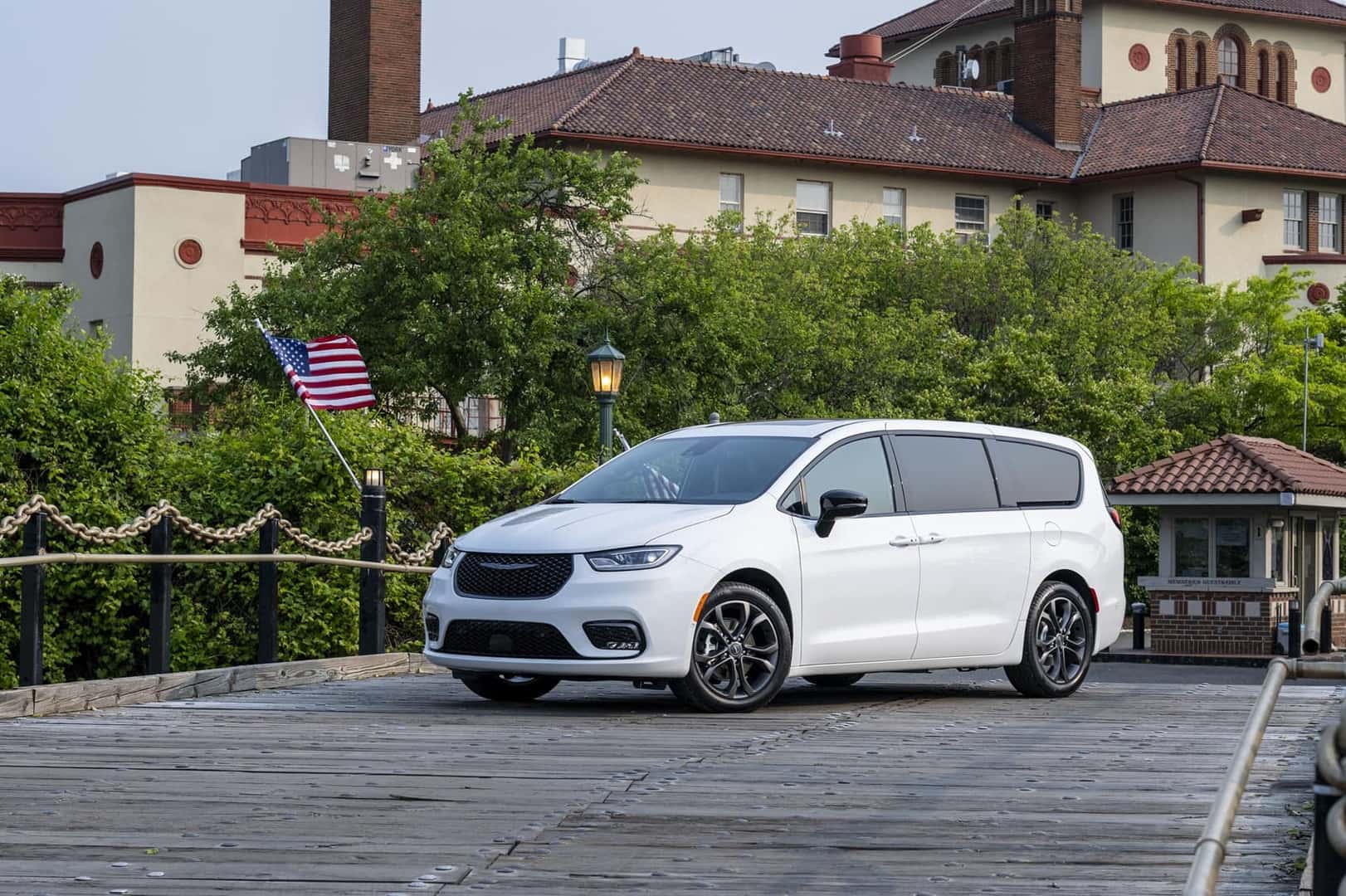 White Chrysler Pacifica parked on a pier heading towards a lake with buildings in the background