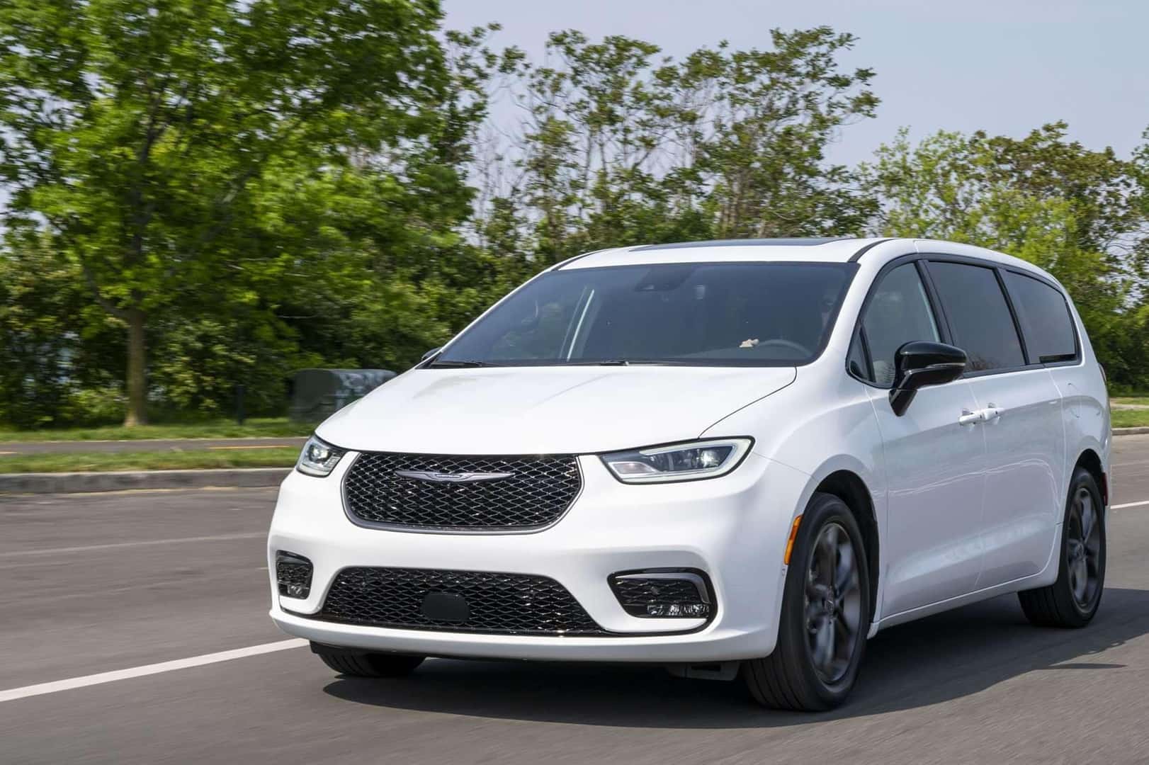 White Chrysler Pacifica traveling on an open road with trees in the background on a sunny afternoon